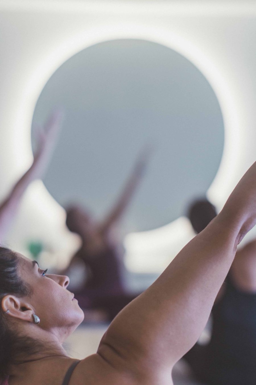 A class with arms raised beneath the studio&rsquo;s circle of light