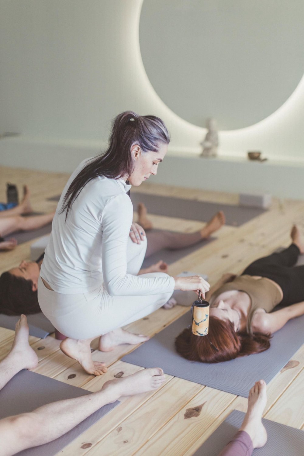 A MyZen teacher kneels beside a student resting on her mat, holding a chime just above her head