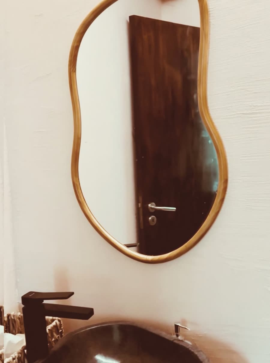 A curved wooden mirror above a stone basin in the washroom