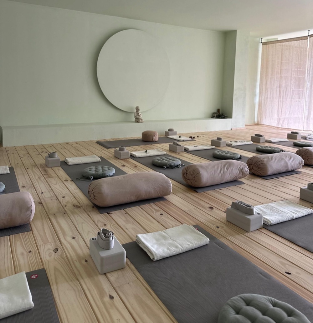The MyZen practice room set for a class: mats with bolsters, cushions, blocks, straps and folded blankets on the wooden floor, the circle on the far wall