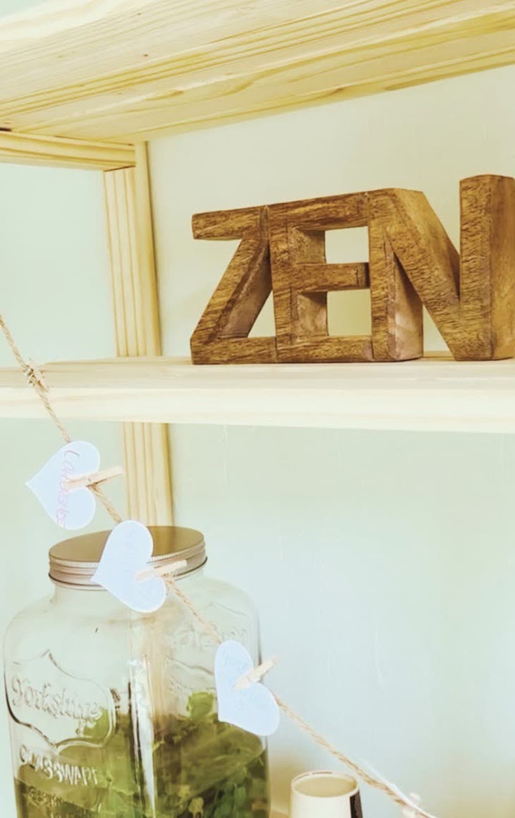The carved ZEN letters on a pine shelf, above a jar of herbal tea