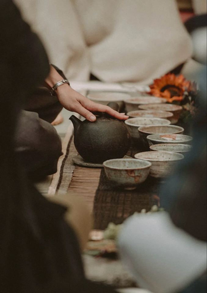 Hands pouring whole-leaf tea into small cups during a ceremony